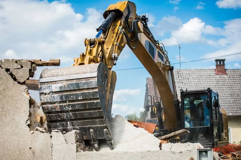 An excavator bucket breaking down a concrete structure