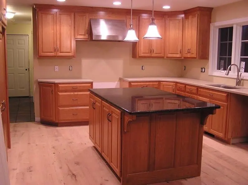 A finished kitchen with wood cabinets, a dark stone island top and pendant lights