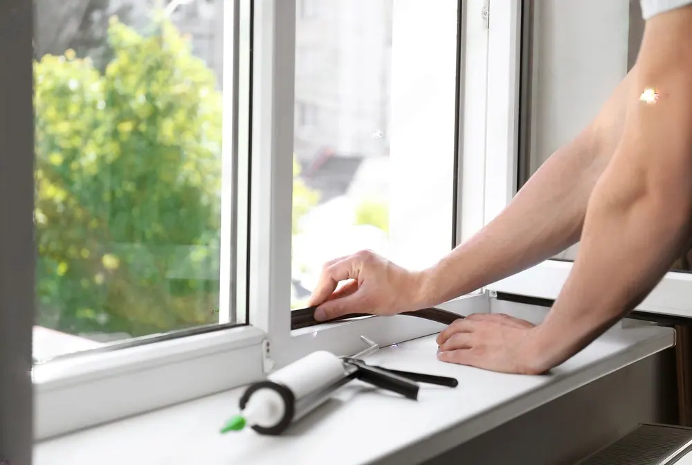 Hands sealing the frame of a new window with a caulk gun on the sill