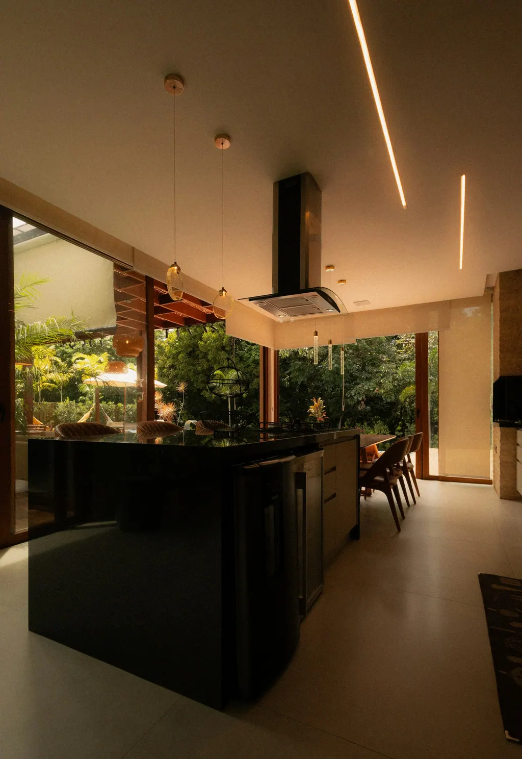A finished kitchen with a dark island under pendant lights and garden views beyond