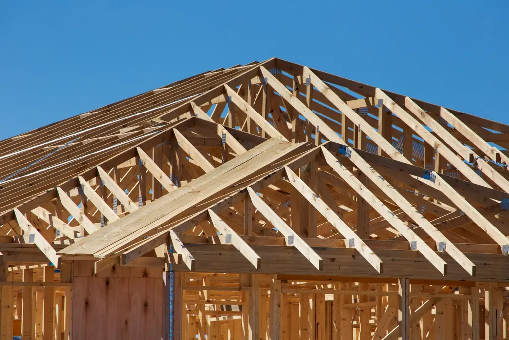The timber frame and roof trusses of a new house under a blue sky